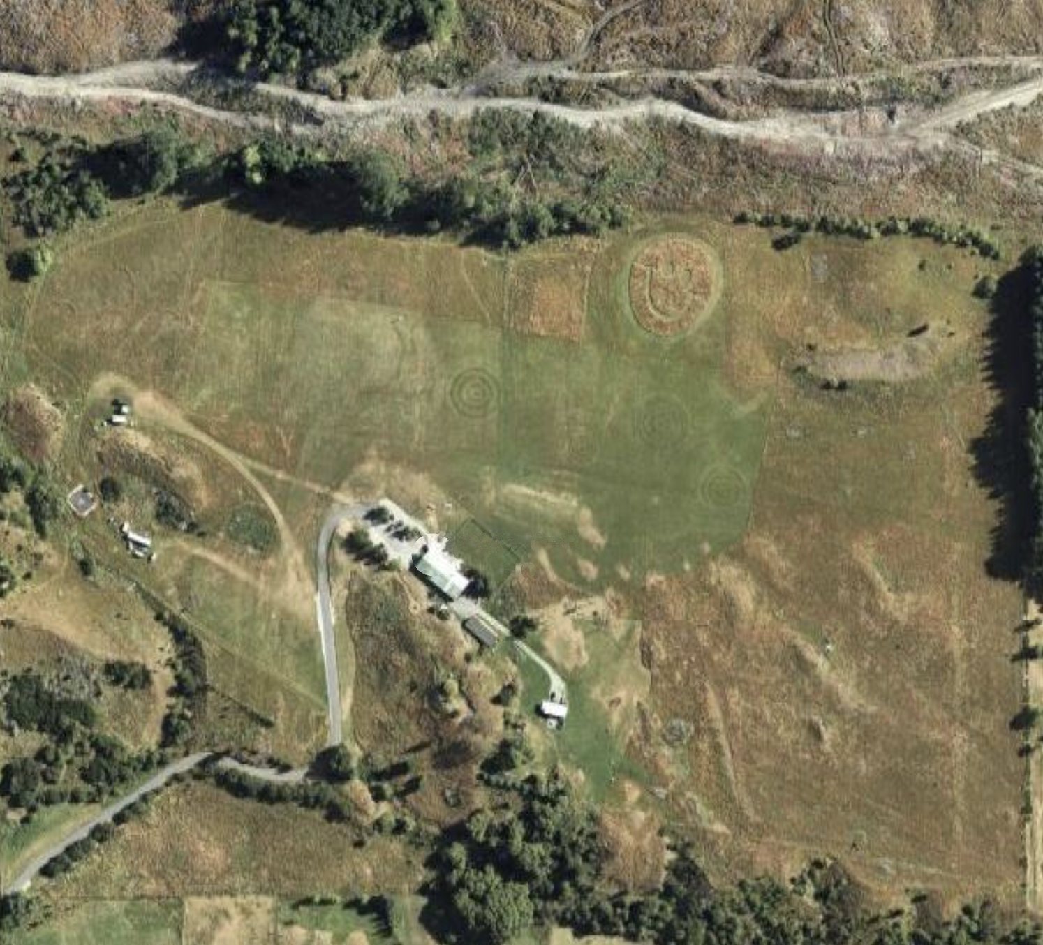 Aerial photo of the Flight Park: a large mown landing field with target rings and a mown smiley face, the HQ buildings and car park on its southern edge, and the access road coming in from the bottom left.